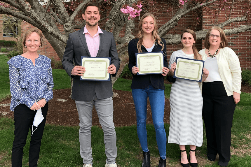 Five people stand outdoors, three of them holding certificates